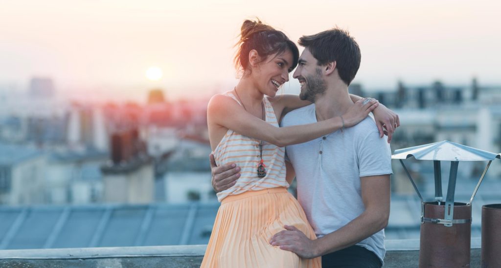 Un couple assis sur un toit qui se prend dans les bras avec le couchée de soleil