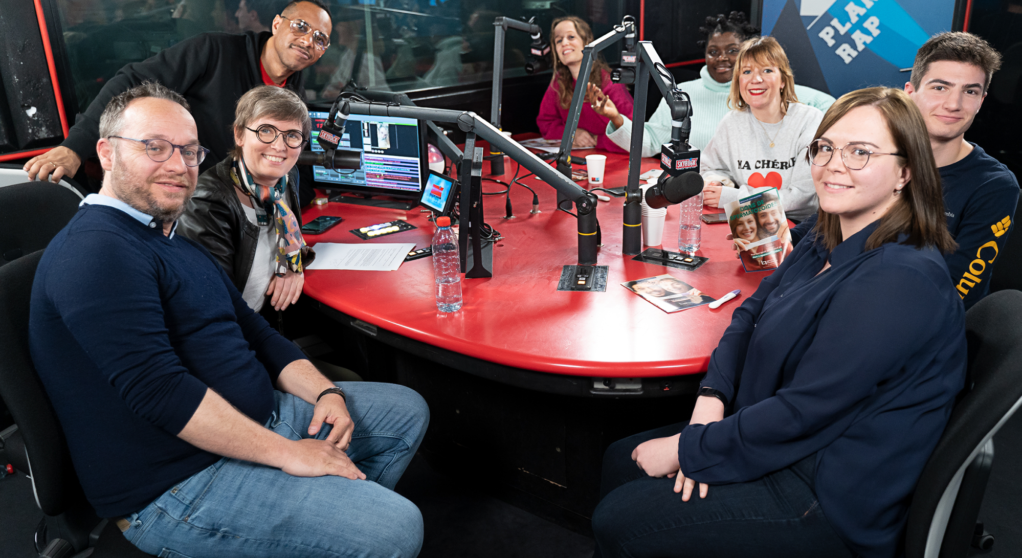 8 personnes avec des micros autour d'une table qui enregistrent une émission sur Skyrock